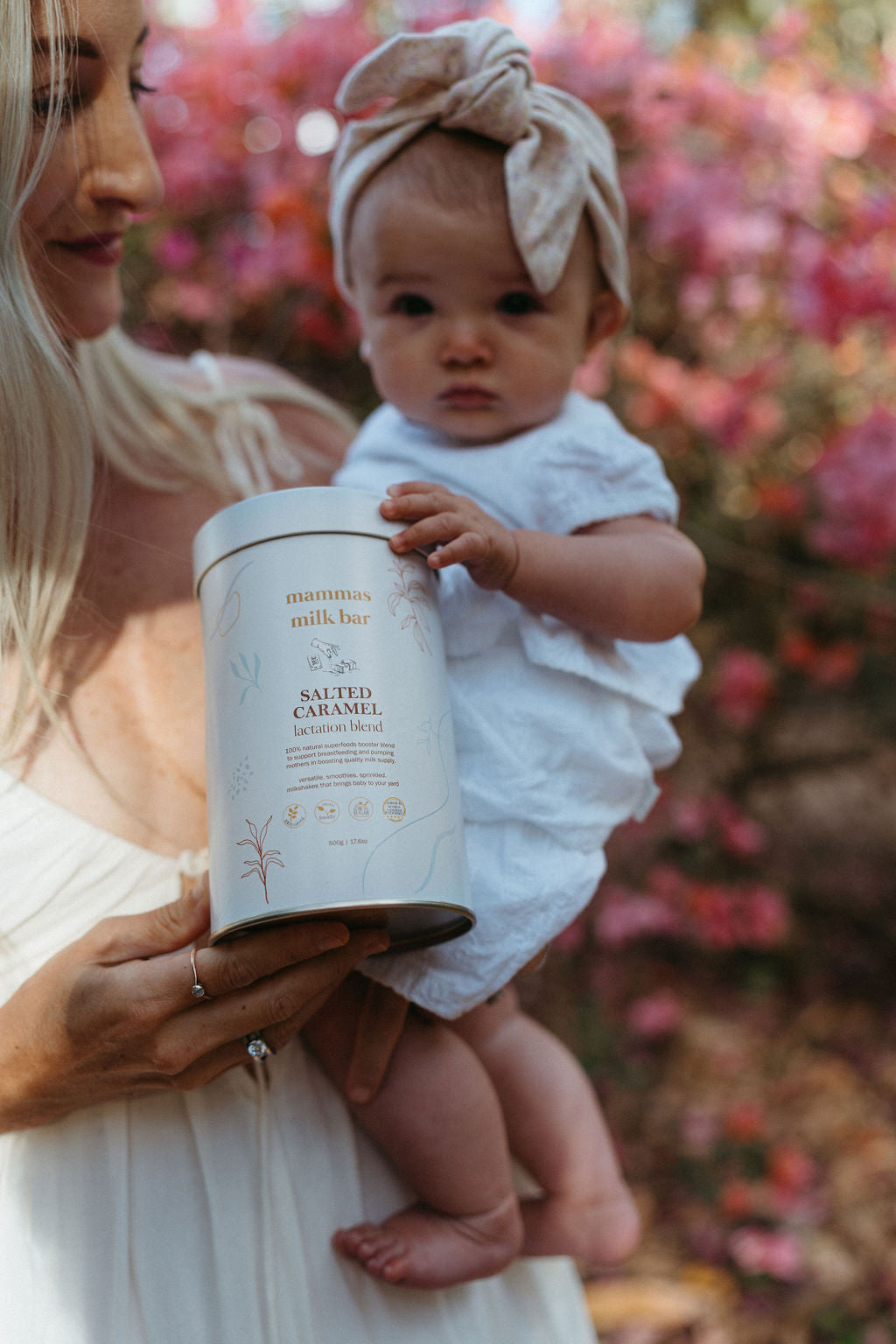 Woman holding a baby and a container labeled 'Sautéed Caramel' against a floral background