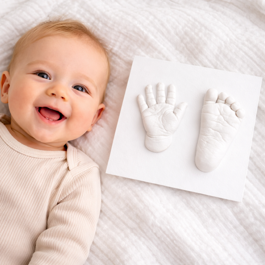 Baby lying next to handprints made with a mold on a soft surface