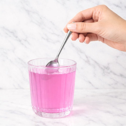 Hand stirring pink liquid in a glass with a spoon on a marble surface